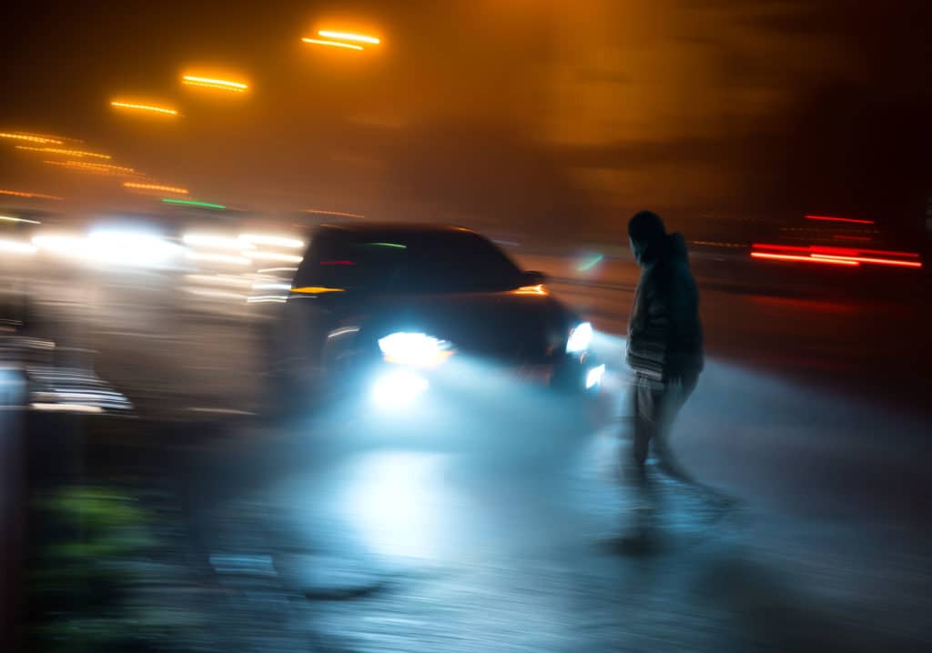 Pedestrian Walking In Front Of Car At Night