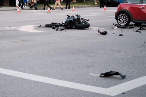 A motorcycle lies wrecked in the road after an accident with a red car.