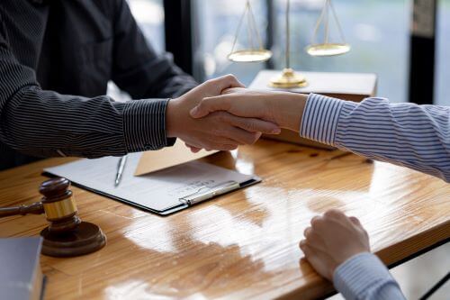 A Port Jefferson personal injury lawyer is shaking hands with a client over his desk.  