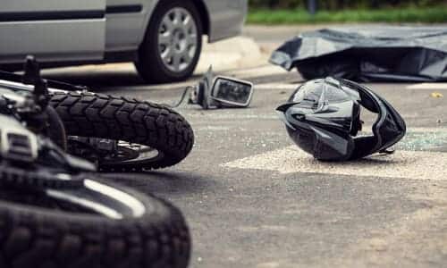 A motorcycle and a black helmet on a road after crashing against a silver-grey sedan on a road.