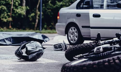 A motorcycle on its side next to a silver car with an open door after a collision between the two.