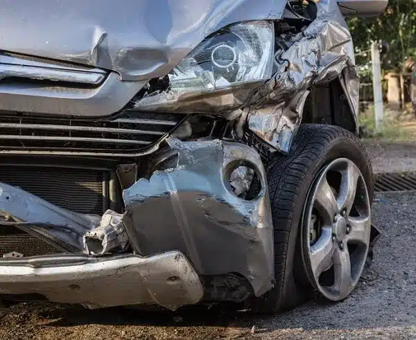 front view of a corner of a vehicle with damaged bonnet, light and a burst tire